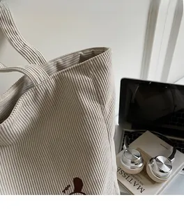 Detail view of corduroy tote bag showing beige ribbed texture and cute brown bear embroidery