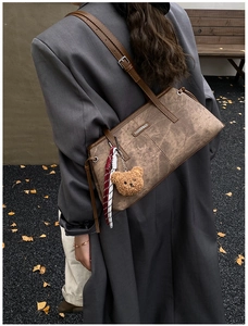 Brown vintage shoulder bag with teddy bear charm and fringe detail in autumn setting