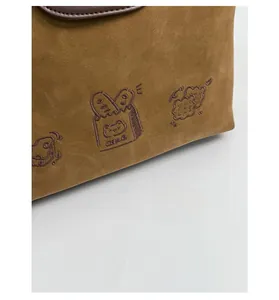 Detail of brown faux suede tote featuring vintage cartoon bread embroidery and leather trim