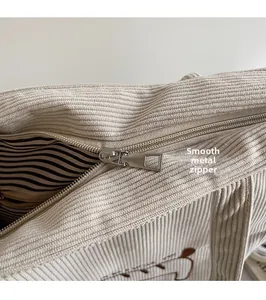 Detail of silver metal zipper on cream corduroy tote bag with striped inner lining