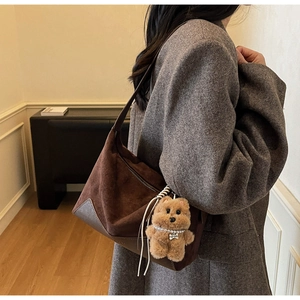 Detailansicht der braunen Wildledertasche mit Plüschbär-Anhänger auf grauem Tweedmantel