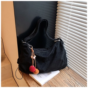 Detail of black corduroy shoulder bag with bohemian pom-pom charm on wooden table