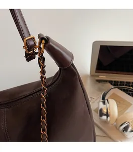 Detail of dark brown leather shoulder bag featuring golden chain and premium stitching