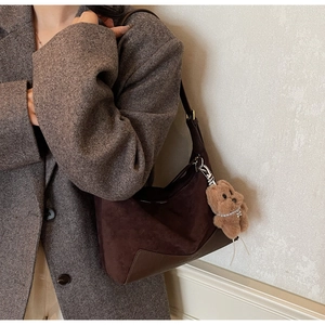 Detail der dunkelbraunen Wildleder-Hobo-Tasche mit Plüschbär-Anhänger an einem Model