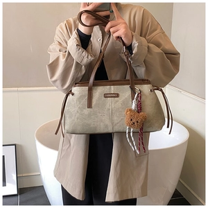Détail du sac en tissu gris-vert avec garniture en cuir brun et breloque ours en peluche