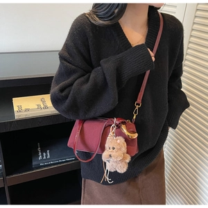 Close-up of vintage burgundy satchel with plush bear charm worn over a black sweater