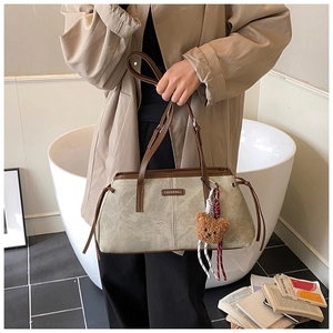 Détail du sac bandoulière en daim gris-vert avec lanières en cuir brun et porte-clé ours