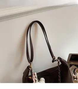 Detail of a dark brown crossbody bag with adjustable strap, metal chain, and cute charms