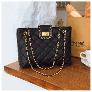 Détail d'un sac cabas en cuir matelassé noir avec fermoir tournant doré et bandoulière chaîne
