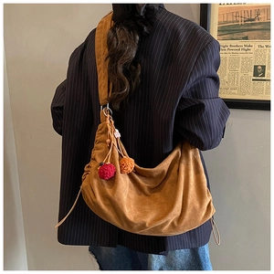 Brown suede hobo bag with colorful pompom charms shown from a side-rear perspective