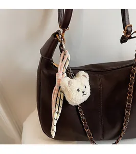 Detail view of a cute cream plush bear charm with a woven strap on a brown leather handbag