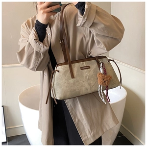 Gros plan du sac beige avec un porte-clés ours en peluche marron et des détails de cordon