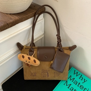 Detail of warm brown suede tote bag with cartoon bread prints and plush charm