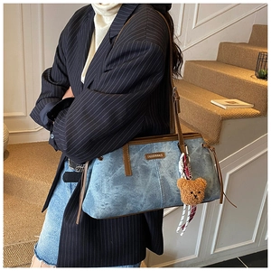 Détail du sac fourre-tout en denim bleu avec garniture en cuir brun et breloque ours
