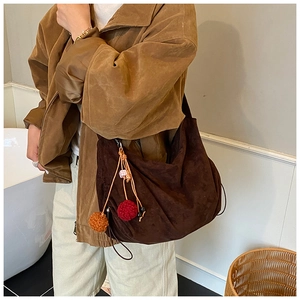 Detail view of a large brown suede hobo bag featuring decorative orange pom-poms on the side