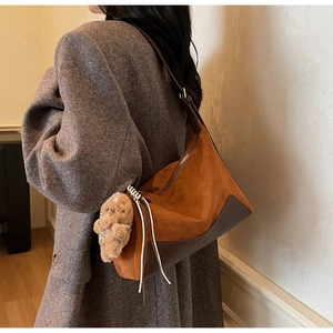 Detail der braunen Wildledertasche mit Bärenanhänger an Modell im Wollmantel