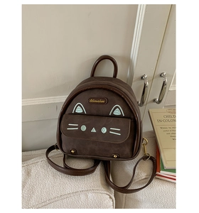 Detail of a brown cat-shaped mini backpack with green embroidery on a soft white sofa
