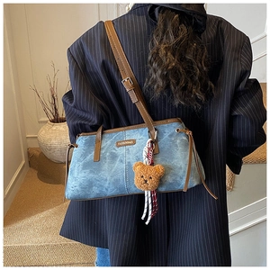 Détail du sac sous le bras en denim bleu avec bordure en cuir brun et breloque