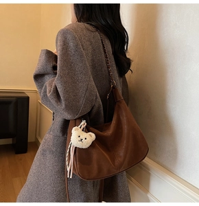 Detail of dark brown leather hobo bag with gold chain strap and cute bear pendant