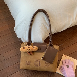 Detail of suede shoulder bag with cartoon bread pattern and leather charm on wood floor