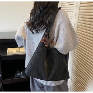 Detail of black matte suede tote bag with brown dachshund charm shown on a model