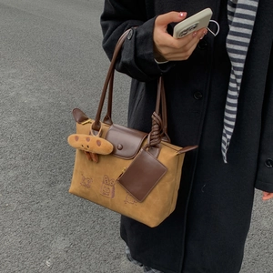 Detail of canvas tote bag with leather handles, cartoon logo, and plush charm