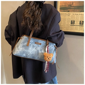 Détail du sac à bandoulière rétro en denim avec bordure en cuir marron et breloque d'ours