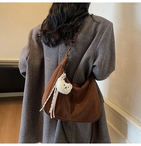 Detail of a brown suede Hobo bag with a vintage metal chain and cute bear plush charm