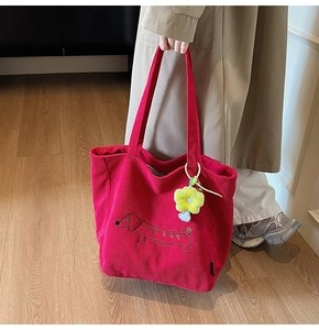 Detail of red corduroy tote bag with cartoon dog embroidery and plush yellow pendant
