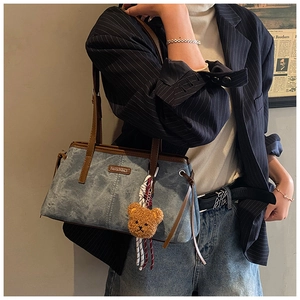 Detail of blue retro shoulder bag with leather strap and plush bear charm on a female model