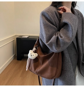 Brown faux leather hobo bag featuring a white plush bear charm and striped ribbon detail