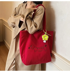 Detail of red corduroy tote bag featuring dachshund embroidery and floral charm on model