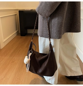 Detail of dark brown hobo shoulder bag featuring plush charm and metallic chain strap