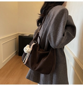 Detail of dark brown dumpling bag with chain strap, soft leather texture and bear charm