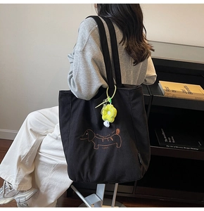Close-up of black corduroy tote bag with dachshund embroidery and a yellow flower charm