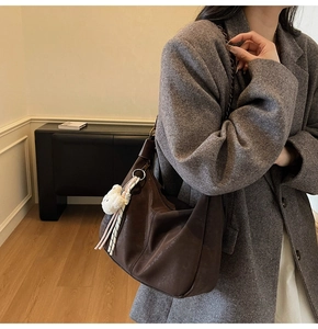 Detail view of deep brown Hobo bag on shoulder with plush bear and metal chain strap