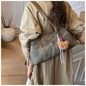 Detail of grey textured shoulder bag with brown leather strap and plush bear pendant