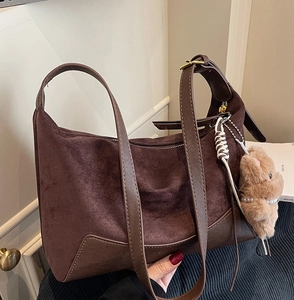 Detail der braunen Wildleder-Beuteltasche mit Glattlederrand und süßem Bärenanhänger