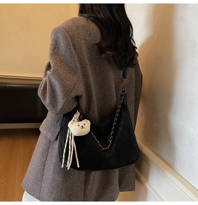 Side view of large black leather hobo bag with chain strap and plush bear charm on model