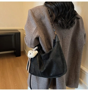 Detail of black semi-circle leather hobo bag with chain strap and teddy bear charm