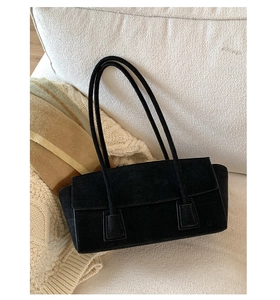 Detail of minimalist black suede shoulder bag with thin straps on a white sofa texture