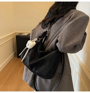 Detail of a large black soft leather dumpling bag with a cute plush bear pendant accessory