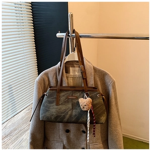Détail d'un sac cabas gris foncé avec lanières en cuir marron et pendentif ours en peluche