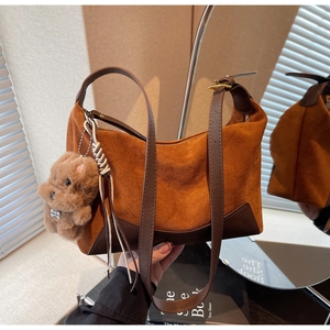 Detailansicht einer braunen Wildleder-Vintage-Tasche mit Plüschbär-Anhänger und Goldschnalle