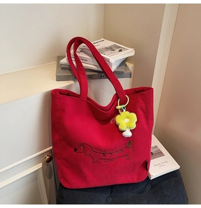 Detailed view of red corduroy tote bag featuring puppy embroidery and flower charm