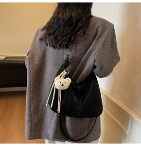Detailed side view of black hobo bag with chain strap and cute bear charm on model