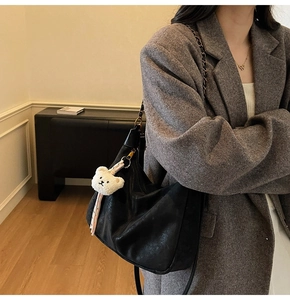 Detail of black leather hobo bag with metal chain strap and white plush bear charm