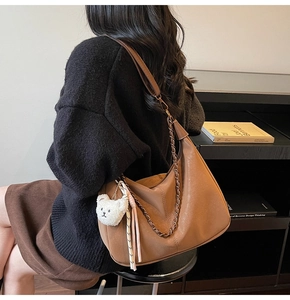 Detail of a brown leather Hobo bag featuring metallic chains and a white teddy bear charm