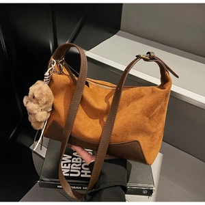 Nahaufnahme der braunen Wildledertasche mit Nähten und einem flauschigen Bärenanhänger
