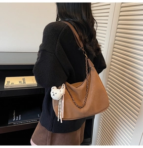 Detail of brown hobo bag with metal chain, leather texture and plush bear charm